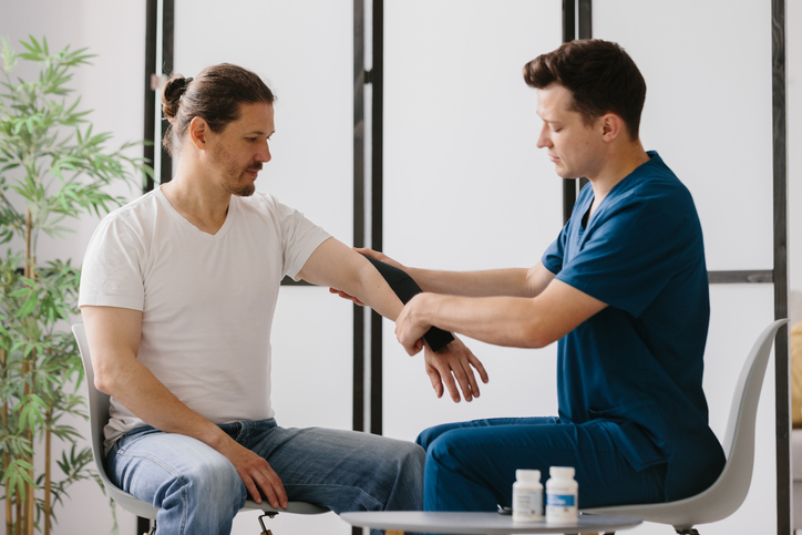 Focused physiotherapist demonstrating kinesiology taping on a patient's forearm.