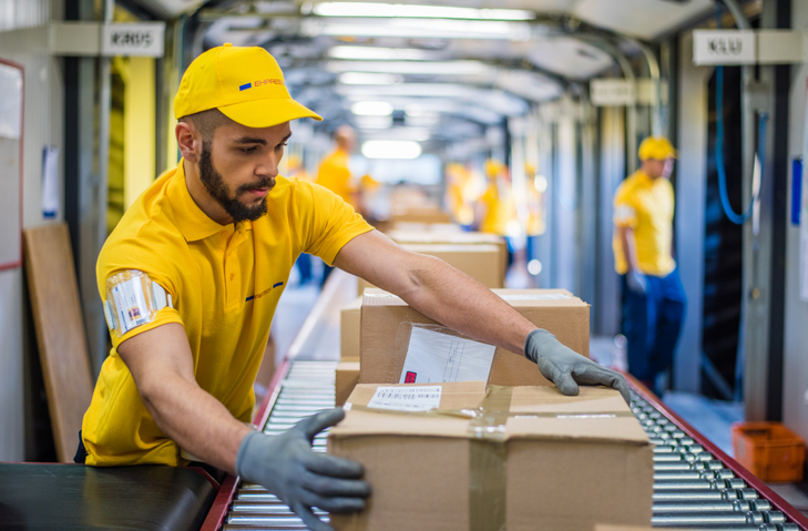 Man processing boxes on conveyor belt in distribution warehouse.