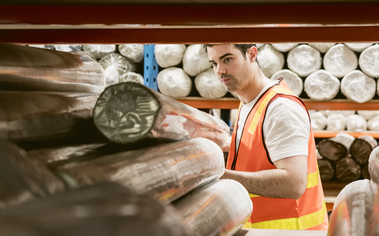 Man wearing high vis removing rolled carpet from shelf in storage facility